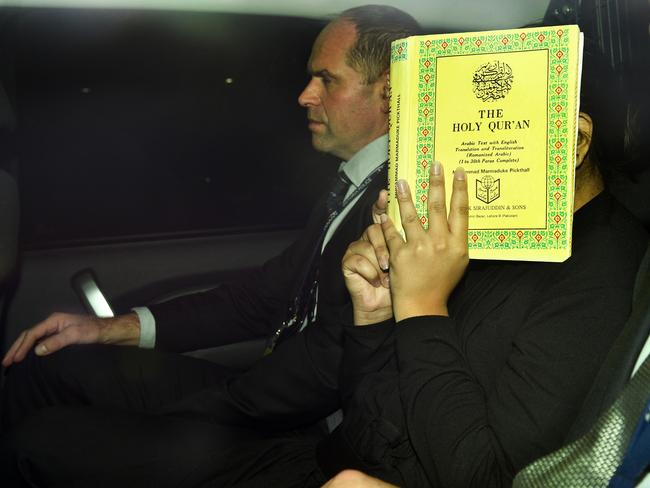 The 22-year-old covers her face with a copy of the Quran while being driven between two detectives. Picture: Mike Keating