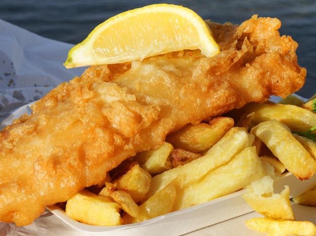 Stock photo showing close-up view of takeaway fish and chips on cardboard tray wrapped in paper with slice of lemon. This is a fish supper being eaten at the seaside with a background of the sea.