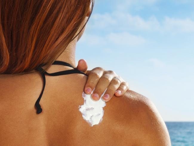 Ð¡ute girl sitting on sandy beach applying sunscreen on her back