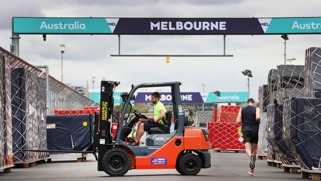 A jogger runs past a forklift driver unpacking Grand Prix team crates on the main straight of Albert Park. Picture: David Caird