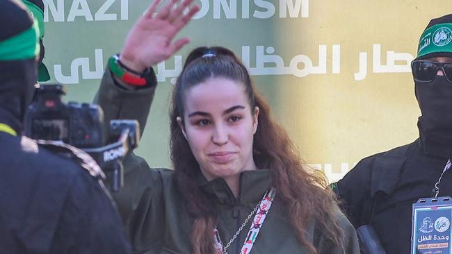 TOPSHOT - Isreali hostage Agam Berger (C) waves as Hamas militants escort her on a stage before handing her over to a Red Cross team in Jabalia on January 30, 2025, as part of their third hostage-prisoner exchange. (Photo by Omar AL-QATTAA / AFP)