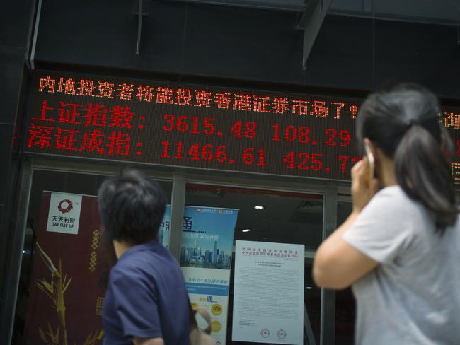 People walk outside of a stock brokerage displaying the values of the Shanghai.