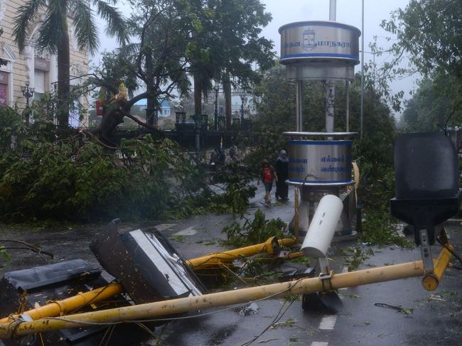 Indian resident stand near debris on a street in Chennai as Cyclone Vardah approaches the Indian coast on December 12, 2016. India on December 12 started evacuating thousands of people from fishing villages as Cyclone Vardah barrelled towards its southeastern coast at speeds of more than 100 kilometres (62 miles) per hour. / AFP PHOTO / Arun SANKAR