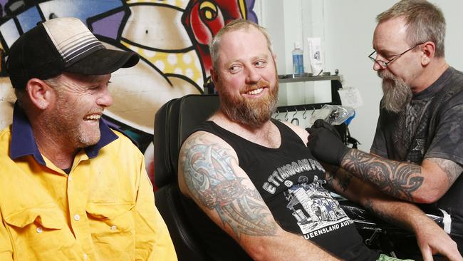 Stuart McEwan applies a bushfire commemoration tattoo to RFS volunteer Rodney McSorley, watched on by brother Darryl. Picture: John Appleyard