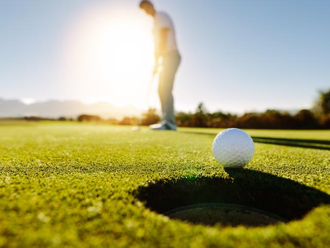 Pro golfer putting golf ball in to the hole. Golf ball by the hole with player in background on a sunny day.