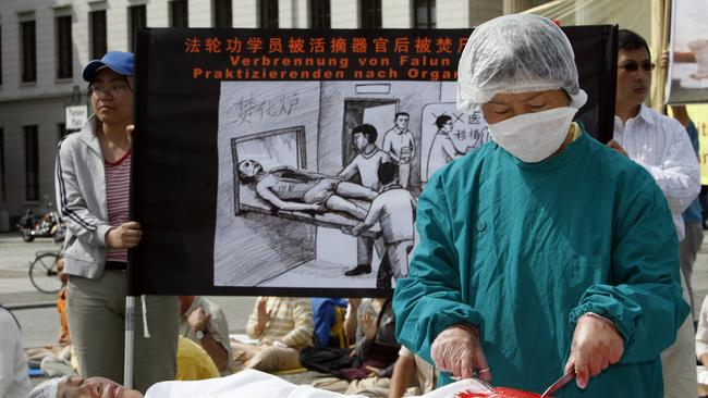 A protester dressed as a Chinese doctor simulates removing organs from another dressed as a Falun Gong practitioner at a Falun Gong protest in Berlin, Germany. Picture: Getty Images