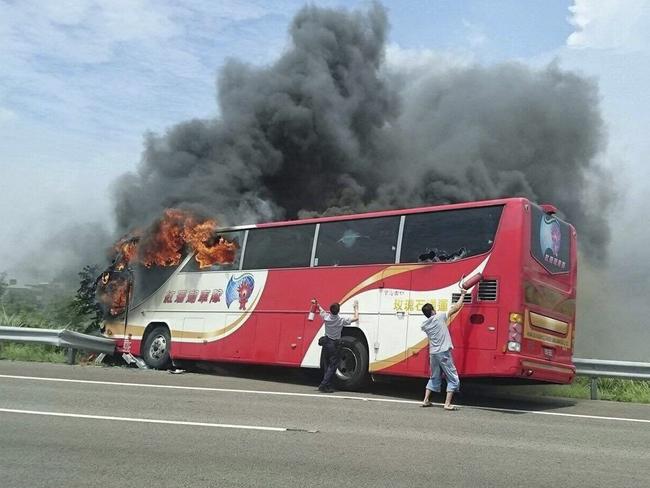 A policeman and another man try to break the windows of a burning tour bus on the side of a highway in Taoyuan, Taiwan, .(Yan Cheng/Scoop Commune via AP)