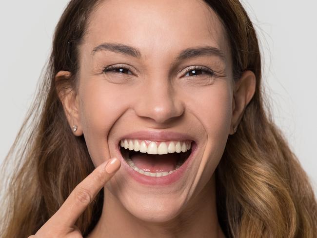 Happy young woman with white straight teeth perfect dent orthodontic smile pointing at tooth looking at camera isolated on studio blank background, dental health stomatology service concept, portrait