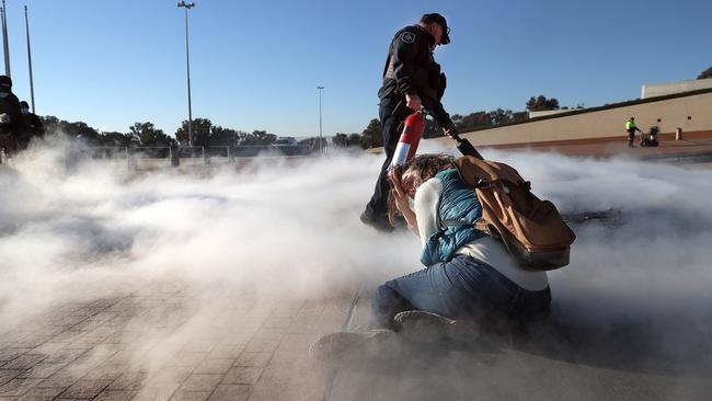 A policeman uses a fire extinguisher to put out a baby's pram that was on fire while a young female protester sits on the forecourt. Picture: NCA NewsWire / Gary Ramage