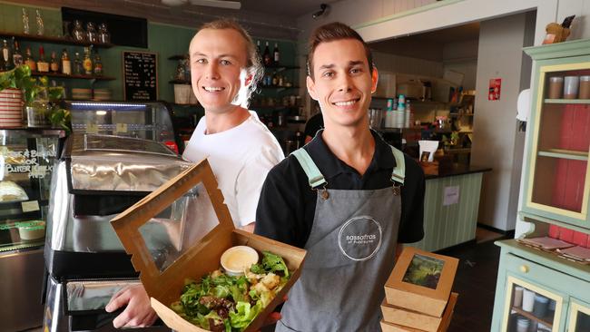 Sassafras kitchen hand Artur Macedo Pedrosa, 27, hands meals over for delivery to community support worker Sam Powderly, 26. Sassafras has made 472 meals for the needy and reopens for general customers from Saturday. Picture: Liam Kidston