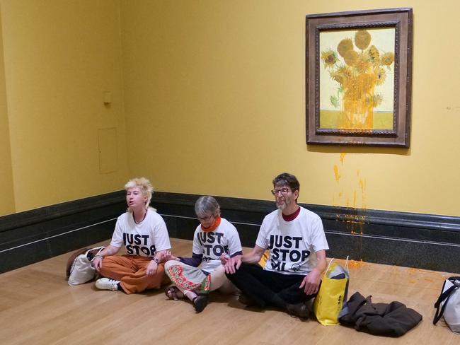 A handout picture from the Just Stop Oil climate campaign group shows three activists sitting on the floor under Vincent van Gogh's "Sunflowers" after throwing tomato soup over two painting's at the National Gallery's  in central London on September 27, 2024, following the sentencing of fellow activists Phoebe Plummer and Anna Holland earlier today. Climate campaigners on Friday hit out at stiff jail sentences given to two activists who threw soup at Vincent van Gogh's "Sunflowers" at a London gallery, voicing fears about the right to peaceful protest. Just Stop Oil protesters Phoebe Plummer, 23, and Anna Holland, 22, were convicted in July of criminal damage after pouring tomato soup over the screen protecting the still life masterpiece at the National Gallery in October 2022. (Photo by Just Stop Oil / AFP) / RESTRICTED TO EDITORIAL USE - MANDATORY CREDIT "AFP PHOTO /  JUST STOP OIL " - NO MARKETING - NO ADVERTISING CAMPAIGNS - DISTRIBUTED AS A SERVICE TO CLIENTS