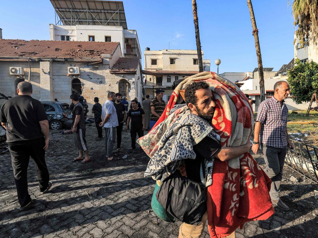 A man walks with salvaged mattresses, pillows, and sheets at the site of the Ahli Arab hospital. Picture: AFP