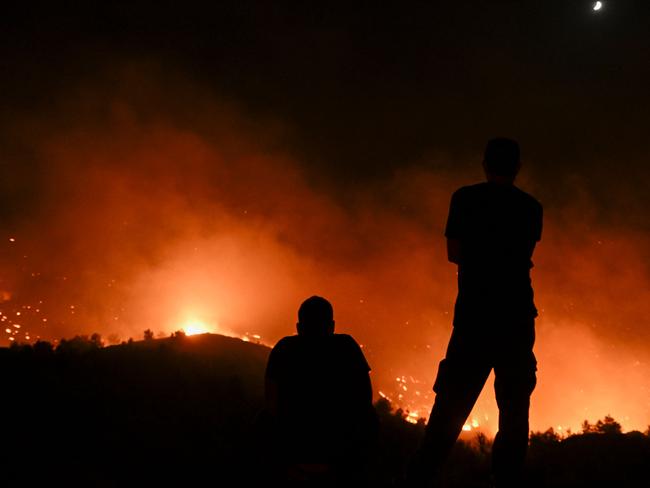 People watch the fires near the village of Malona in the Greek island of Rhodes on July 23, 2023. Tens of thousands of people fled wildfires on the Greek island of Rhodes on July 23, 2023, as terrified tourists scrambled to get home. Firefighters tackled blazes that erupted in peak tourism season, sparking the country's largest-ever wildfire evacuation -- and leaving flights and holidays cancelled. (Photo by SPYROS BAKALIS / AFP)