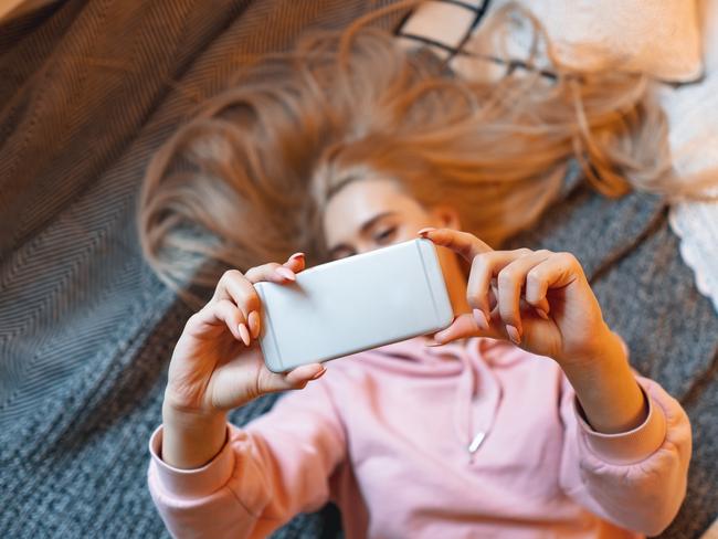 Pretty young girl having fun, making selfie while lying on the bed at home. Top angle view. Charming Caucasian woman taking picture of herself, for her friends and fans, for social media. Picture: Istock