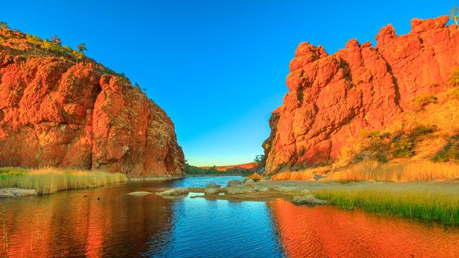 NRM ESCAPE Northern Territory, Australian Outback. Scenic Glen Helen Gorge in West MacDonnell Ranges changes colours with sunrise light and reflects on waterhole in dry season at sunrise light.