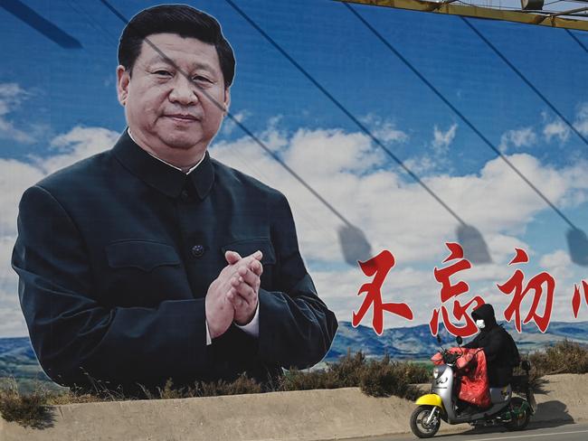 A man rides a scooter past a billboard showing Chinese President Xi Jinping with a slogan which reads "Remain true to our original aspiration and keep our mission firmly in mind" in Beijing on February 28, 2023. (Photo by Jade Gao / AFP)