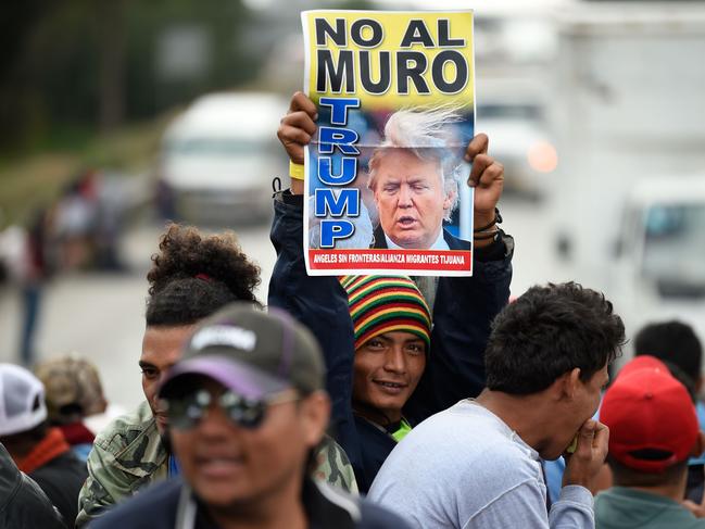 TOPSHOT - A migrant travelling with fellow migrants from poor Central American countries -mostly Hondurans- towards the United States in hopes of a better life or to escape violence, shows a banner reading "No to the Wall" and showing a picture of US President Donald Trump, rides on the back of a truck as they leave the Mexican capital to continue their trek north, on November 10, 2018. - The United States embarked Friday on a policy of automatically rejecting asylum claims of people who cross the Mexican border illegally in a bid to deter Central American migrants and force Mexico to handle them. (Photo by Alfredo ESTRELLA / AFP)