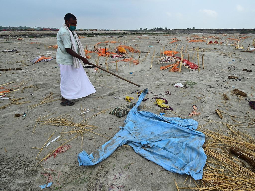 A man uses a stick to move a PPE suit lying amid human remains. Picture: AFP