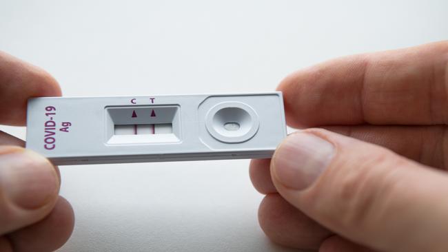 Rapid antigen detection test (RADT) with two red stripes showing a POSITIVE result of a human sample testing. Mans fingers holding the white plastic device with a COVID-19 Ag inscription.