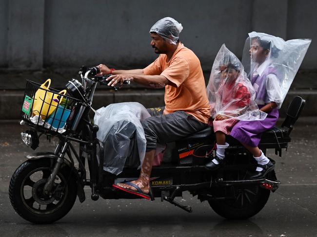 Children are protected with plastic sheets for a motorbike ride during monsoon rainfall in Hyderabad, India. Picture: Noah Seelam / AFP