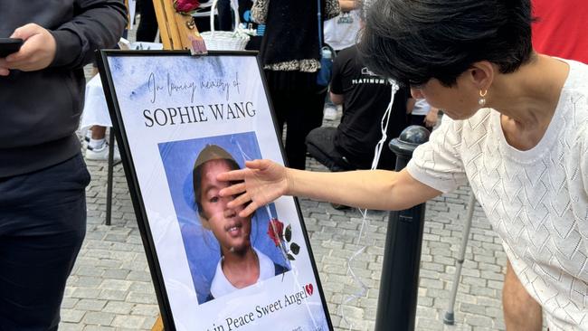 A woman touches the photograph of Gold Coast schoolgirl Sophie Wang at her candlelight vigil at Carrara on August 16, 2024. Photo: Kathleen Skene