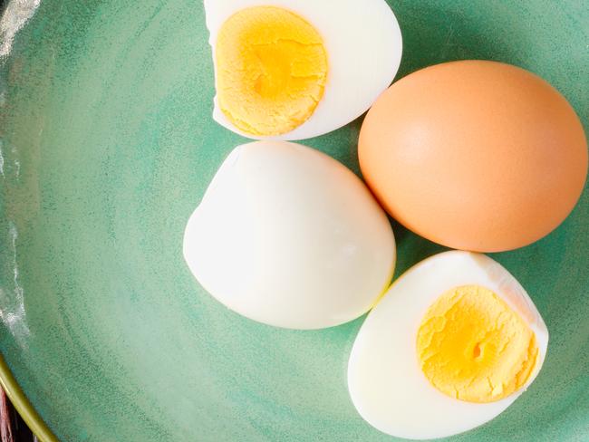 Hard-boiled egg cut and piled on egg slicer and full egg with shell on green plate or dish.