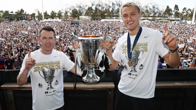 Collingwood coach and new father Craig McRae, left, holds the premiership cup aloft with captain Darcy Moore at Olympic Park on Sunday. Picture: Michael Klein