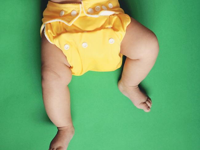 Stock photo of a five month old Baby wearing yellow cloth nappy or diaper (reusable diaper) against green background. Picture: Getty Images