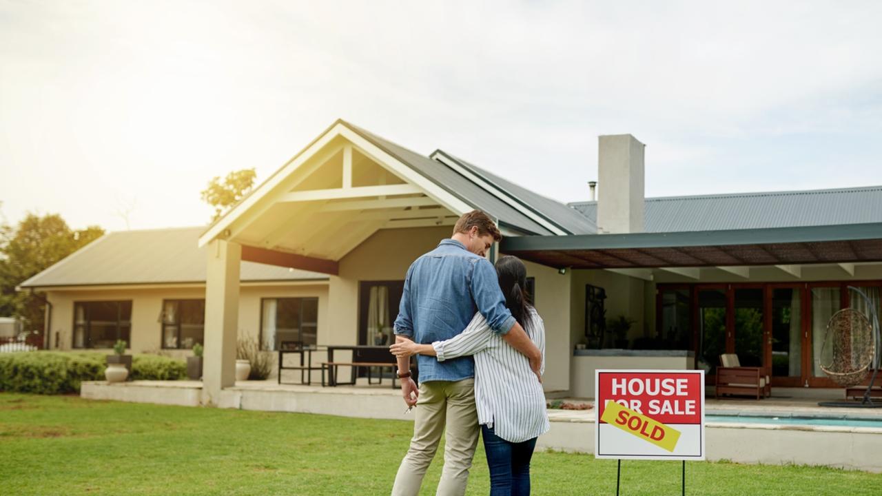 Shot of a couple standing next to a real estate sold sign at their new house