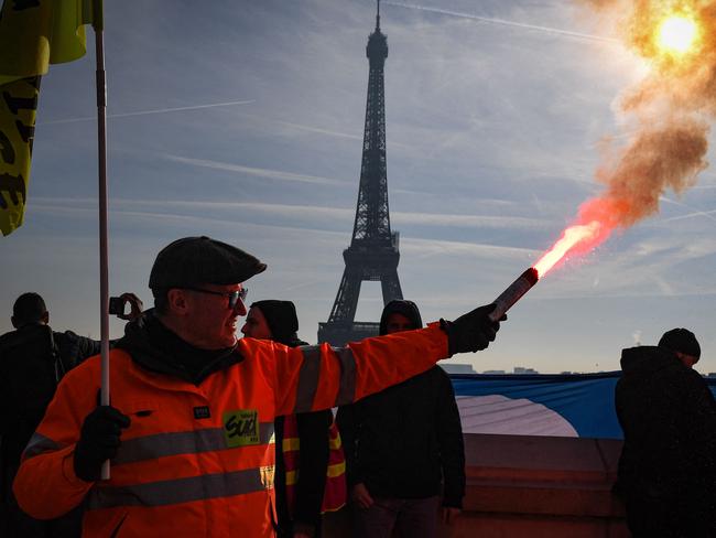 A members of the SUD labour union holds a flare during a demonstration on the Parvis du Trocadero, across the Seine river from the Eiffel Tower, during a cross-sector labour union protest against France's controversial pension reform bill, in Paris, on February 9, 2023. - The planned reforms include hiking the retirement age from 62 to 64 and increasing the number of years people must make contributions for a full pension. (Photo by Alain JOCARD / AFP)