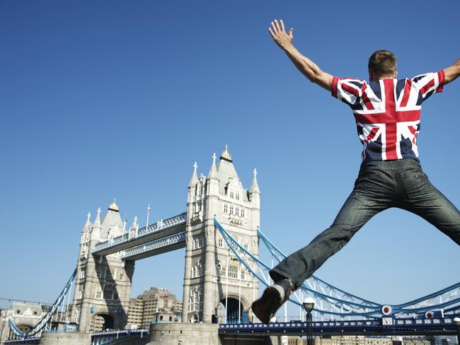 Man in Union Jack (UK flag) t-shirt jumping in front of bright view of London skyline at Tower Bridge