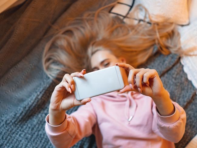 Pretty young girl having fun, making selfie while lying on the bed at home. Top angle view. Charming Caucasian woman taking picture of herself, for her friends and fans, for social media. Picture: Istock
