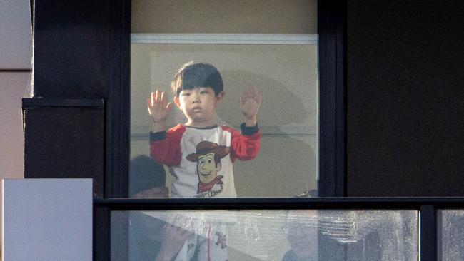 Self-isolating residents take a glimpse at the outside world from their Ariele apartment complex flat in Maribyrnong, in Melbourne’s northwest. Picture: Aaron Francis