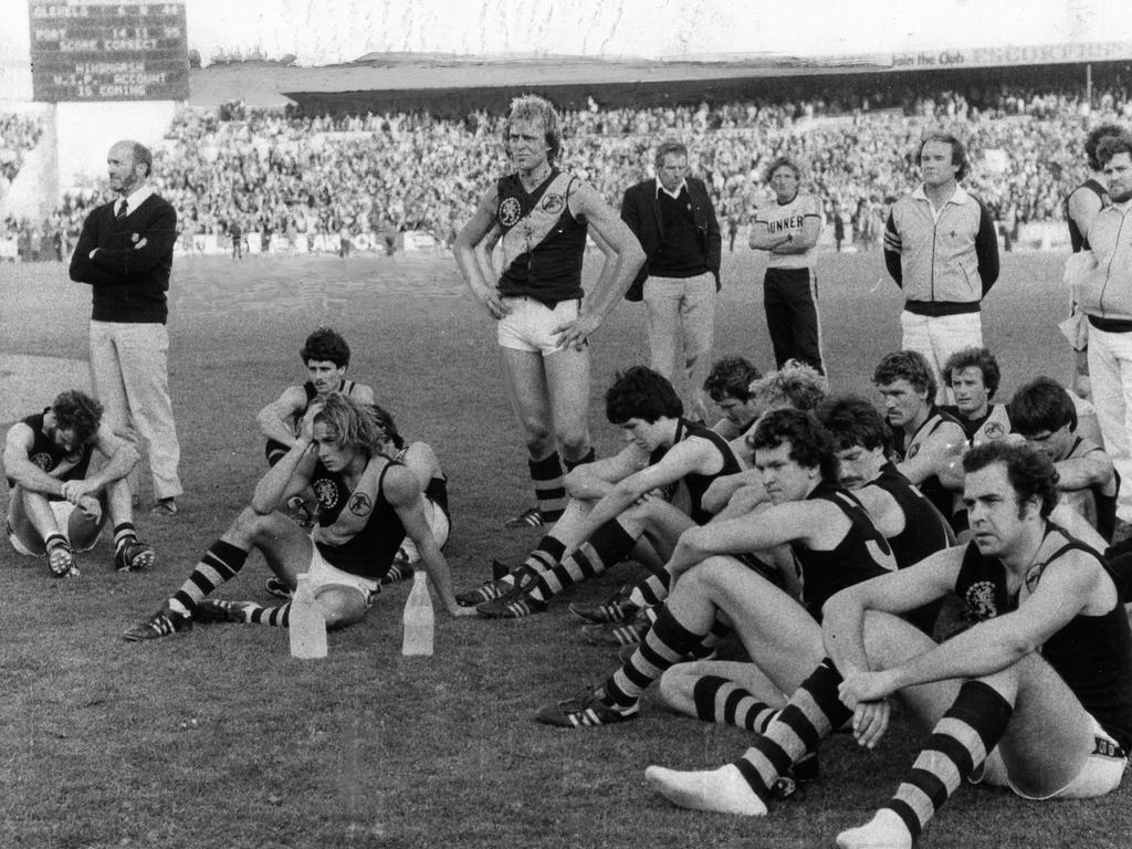 Disappointed Glenelg players including Graham Cornes (standing) watch as Port are presented with the premiership flag.