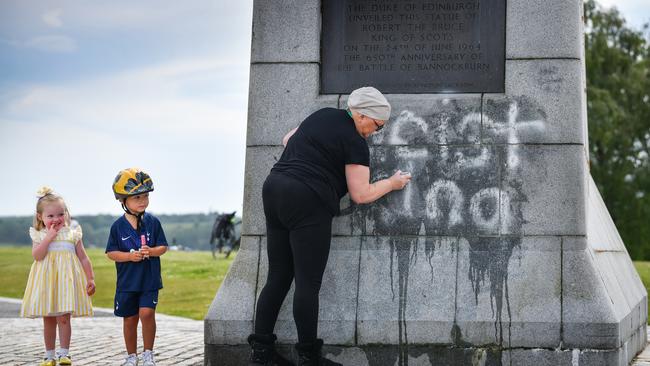 Children look on as a member of the public cleans the Robert the Bruce statue which has been defaced with graffiti saying "racist king" in Bannockburn, Scotland.