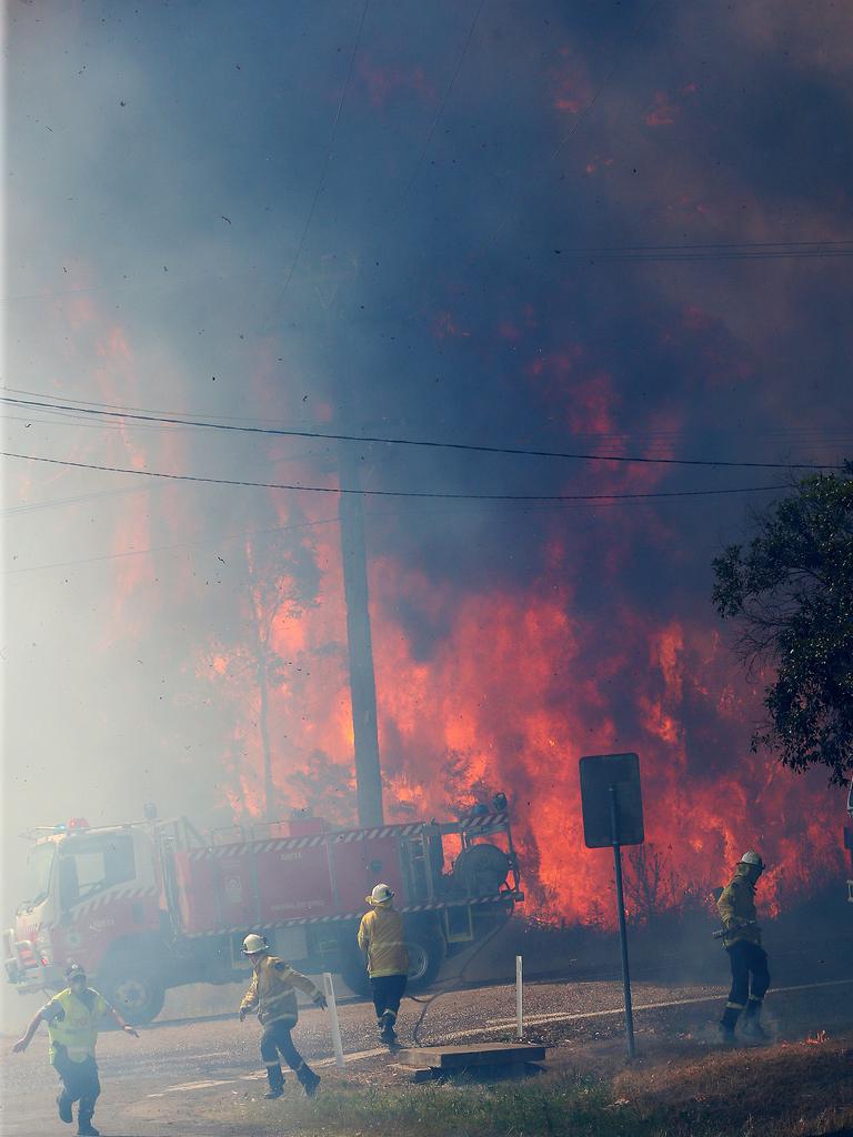 Firefighters and police run from a fire engine as an out-of-control bushfire jumps Wine Country Drive, north of Cessnock. Picture: Peter Lorimer