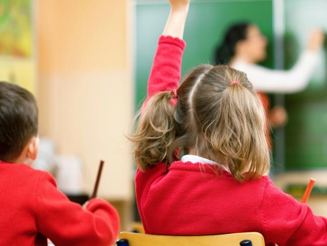 Elementary school kids raising their hands in class to answer a teacher's question.