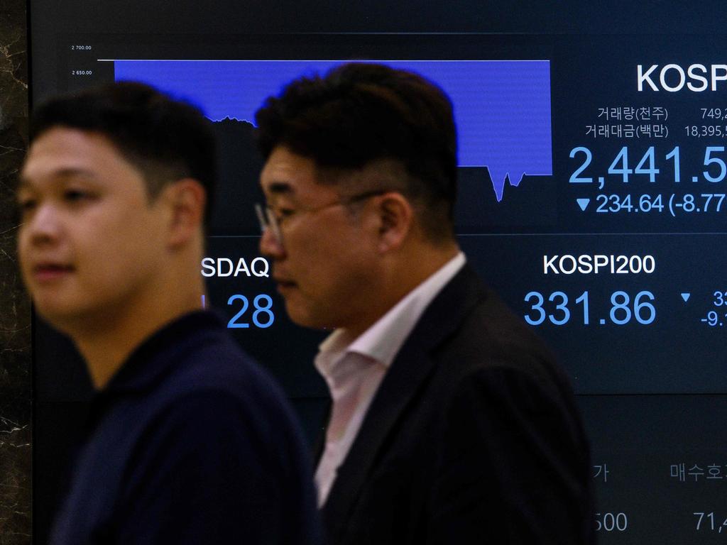 People walk past a monitor displaying the benchmark Kospi index after the close of trading in Seoul on August 5, 2024. Seoul's stocks plunged more than eight per cent at closing, after weak US jobs data fanned fears of a recession in the world's top economy and boosted bets on several Federal Reserve interest rate cuts. (Photo by ANTHONY WALLACE / AFP)