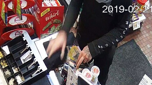 CCTV image of an armed robber, with a distinctive tattoo on the back of his left hand, grabbing cash from the till while holding up the Budget Service Station on Harbord Rd, Freshwater. Source: NSW Police