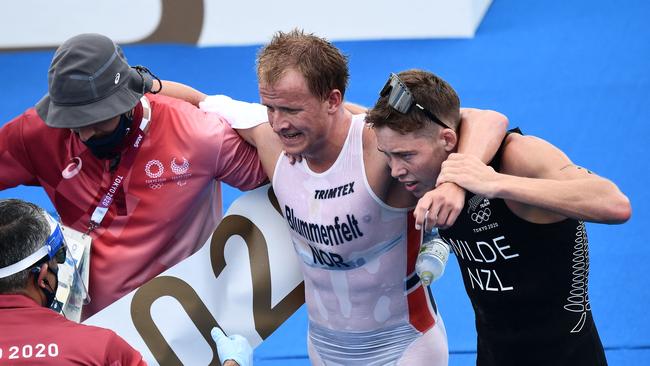 Norway's Kristian Blummenfelt is helped by New Zealand's Hayden Wilde (R) and an official at the end of the men's individual triathlon.