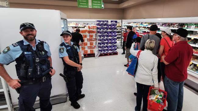 Police officers watch as people queue for a delivery of toilet paper and pasta at a Coles supermarket in Epping in Sydney last week..