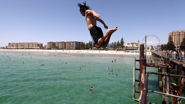 Teens jump of the jetty at Glenelg Beach during a hot day in Adelaide. Picture: AAP Image/Kelly Barnes