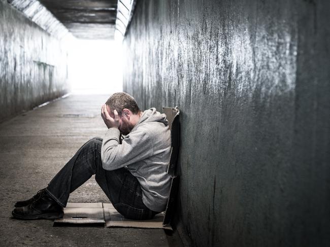 Young homeless male of caucasian ethnicity sitting on the floor of a dark subway tunnel with his hands on his head. Desaturated horizontal colour image with lots of room for copy space. LEV pg 8-9homeless man tunnel 2 iSTOCK