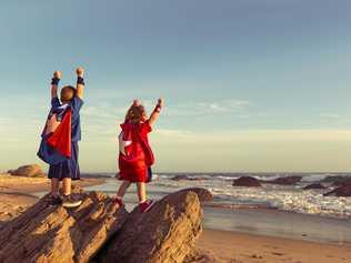 A young boy and girl dressed as a superheroes stands on a rock with arms raised while on a California Beach. The surf and waves wash the sand around them and they are ready to work as a team to accomplish great things as they look out to sea. Image taken in Orange County, California, USA. Picture: RichVintage