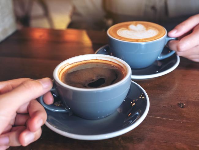 Close up image of a man and a woman clinking blue coffee mugs on wooden table in cafe