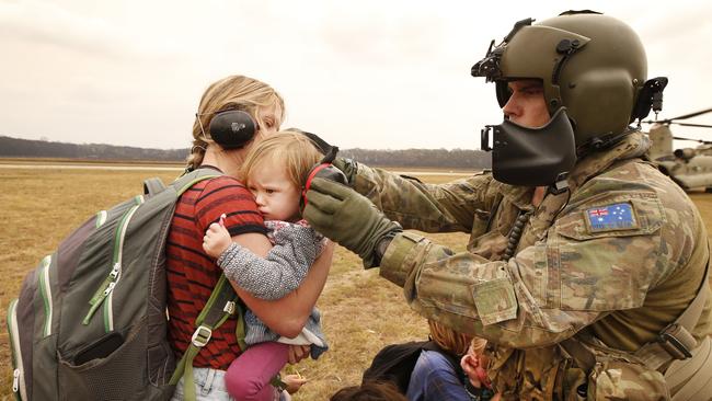 An Army Chinook crew member tries to comfort a distressed child while fitting ear protection before boarding the running Chinook helicopter bound for Sale. Picture: David Caird