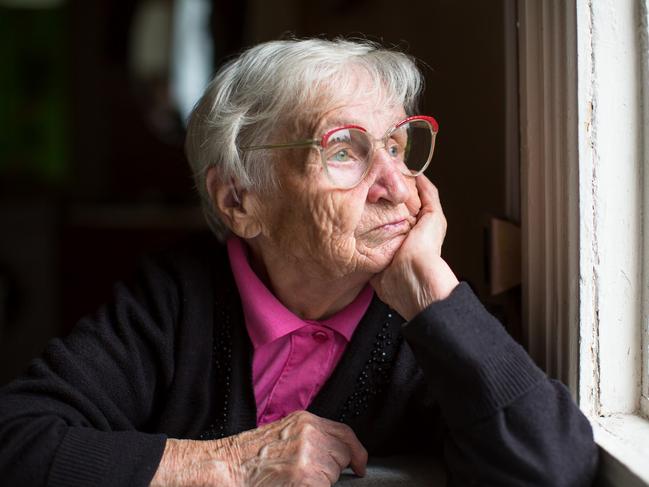 Elderly woman in glasses thoughtfully looking out the window.