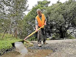 DIGGING IN: Councillor David Yarnall shovelling water from a 10cm deep pothole on Keerong Rd at The Channon. He has suggested giving residents the equipment to fix roads themselves to speed up the rate of repairs. Doug Eaton