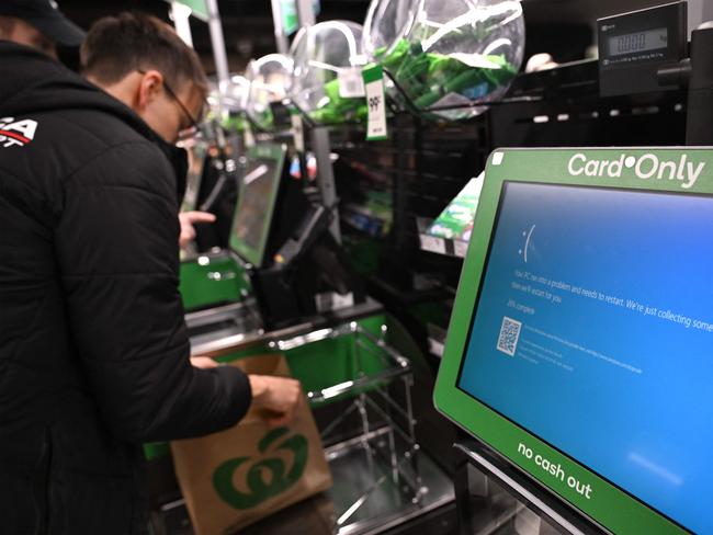 A customer takes care of his shopping next to blue screen at self-checkout terminals of a supermarket in Sydney on July 19, 2024. A large-scale outage wrought havoc on IT systems across Australia, with the country's national broadcaster, its largest international airport and a major telecommunications company reporting issues. (Photo by Saeed KHAN / AFP)