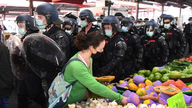 A woman continues to shop for vegetables as riot police clear Melbourne's Queen Victoria Market of anti-lockdown protesters. Picture: AFP